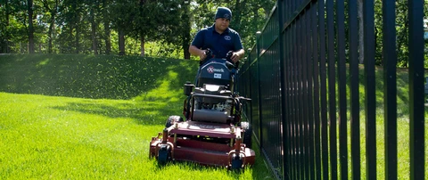 Hambleton Lawn & Landscape professional mowing a lawn beside a gate in Manassas, VA.