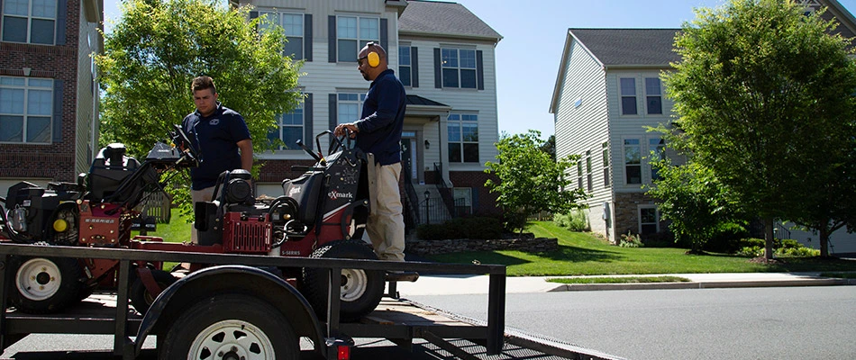 A trailor with two workers unloading a lawn mower and aerator in Arlington, VA.